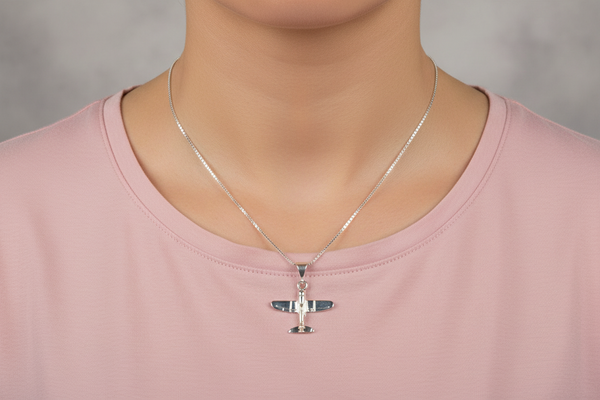 Silver airplane pendant necklace on a pink shirt against a neutral background