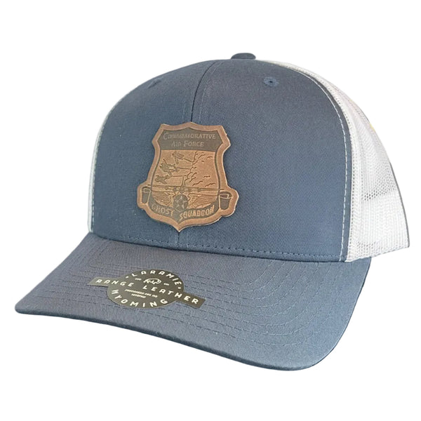 A blue and white trucker hat with a brown leather shield patch on the front.